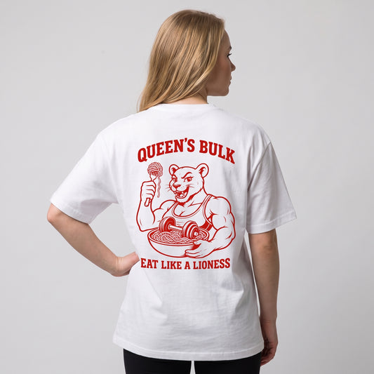 Female model wearing the white KING APEX Queen’s Bulk oversized T-shirt, back view with one hand on the hip showing the red lioness eating pasta with QUEEN’S BULK and EAT LIKE A LIONESS lettering.