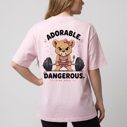 Female model wearing the soft pink KING APEX Adorable. Dangerous. oversized T-shirt, showing the cartoon lioness lifting a barbell on the back.