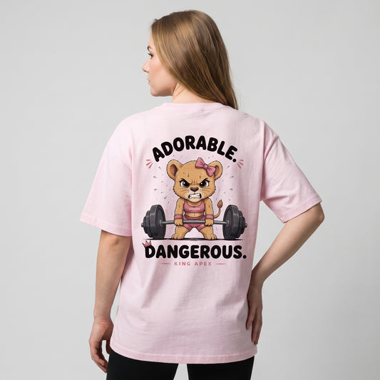 Female model wearing the soft pink KING APEX Adorable. Dangerous. oversized T-shirt, showing the cartoon lioness lifting a barbell on the back.