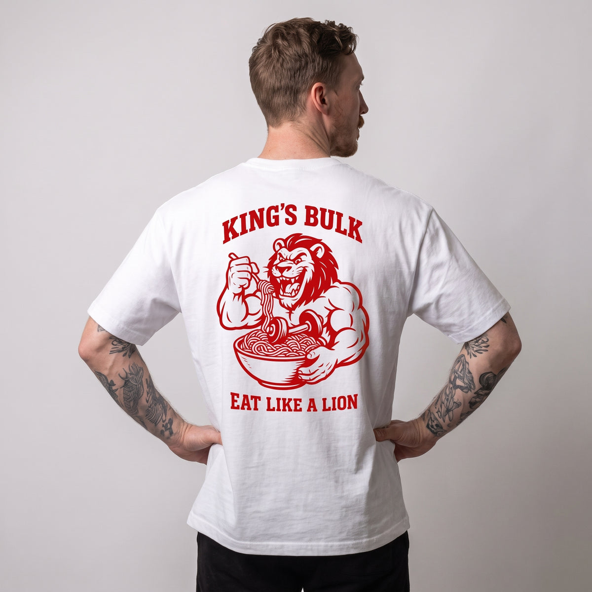 Male model wearing the white KING APEX King’s Bulk oversized T-shirt, back view with hands on hips showing the red lion eating pasta with KING’S BULK and EAT LIKE A LION lettering.