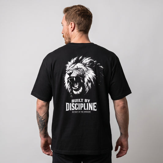 Male model wearing the black KING APEX Lion Built by Discipline oversized T-shirt, back view showing the white roaring lion portrait with BUILT BY DISCIPLINE lettering.