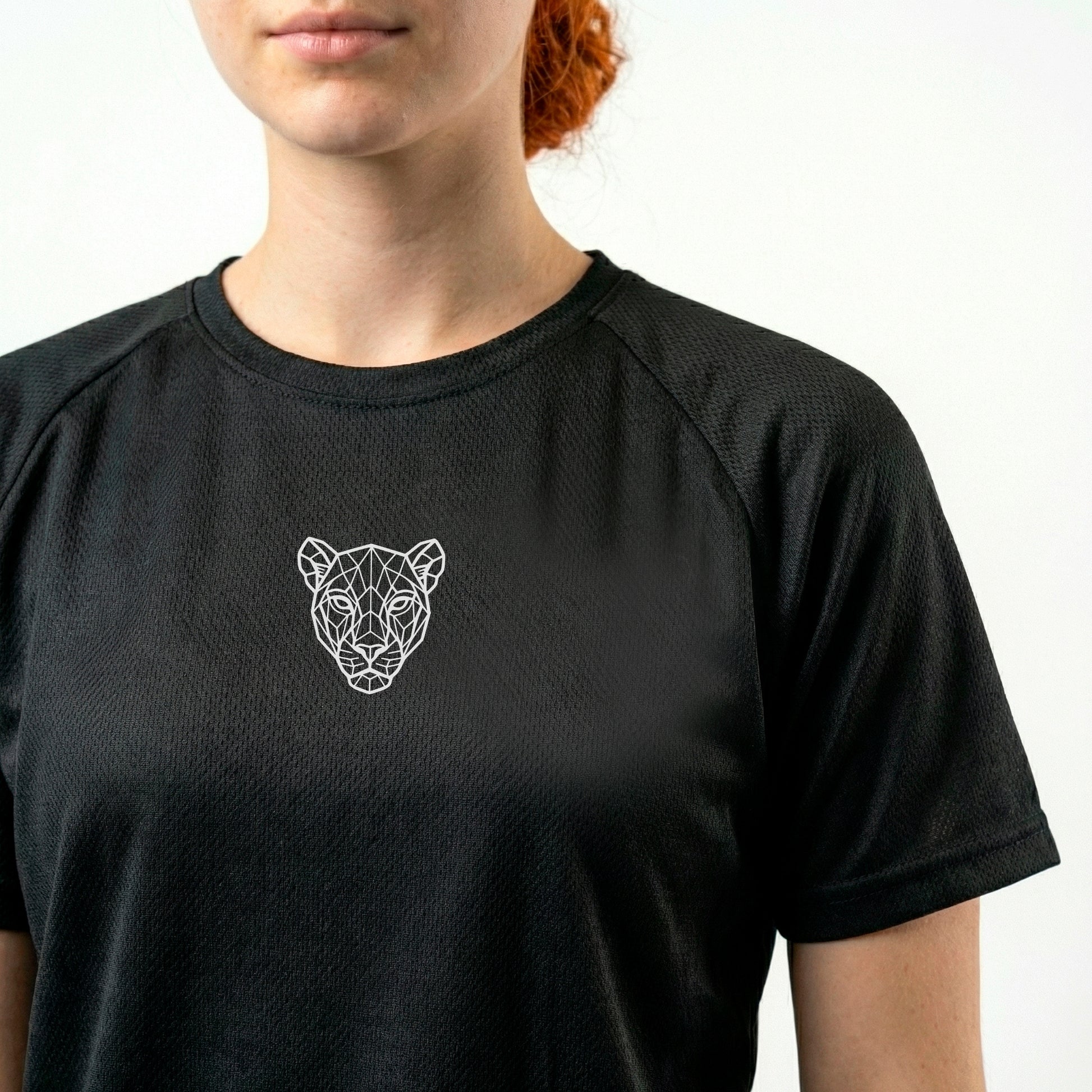 Close-up of minimal lioness logo on KING APEX black sports jersey showing fabric texture and chest detail