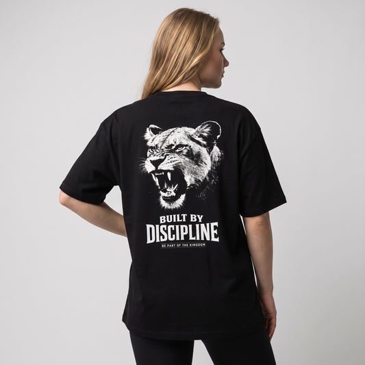 Female model wearing the black KING APEX Lioness Built by Discipline oversized T-shirt, back view showing the white roaring lioness portrait with BUILT BY DISCIPLINE lettering.