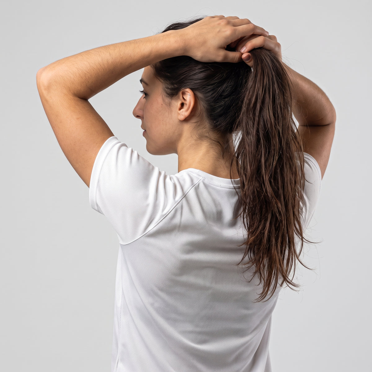 Back view of woman wearing the white KING APEX Lioness sports jersey while tying her hair.