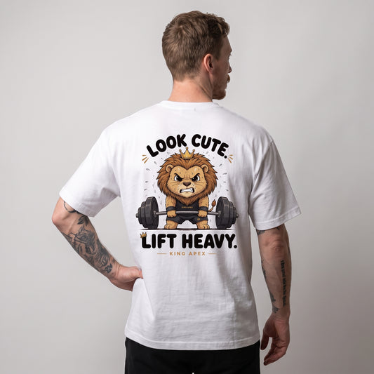 Male model wearing the white KING APEX Look Cute. Lift Heavy. oversized T-shirt, back view with one hand on the hip showing the crowned cartoon lion lifting a barbell with LOOK CUTE. LIFT HEAVY. lettering.