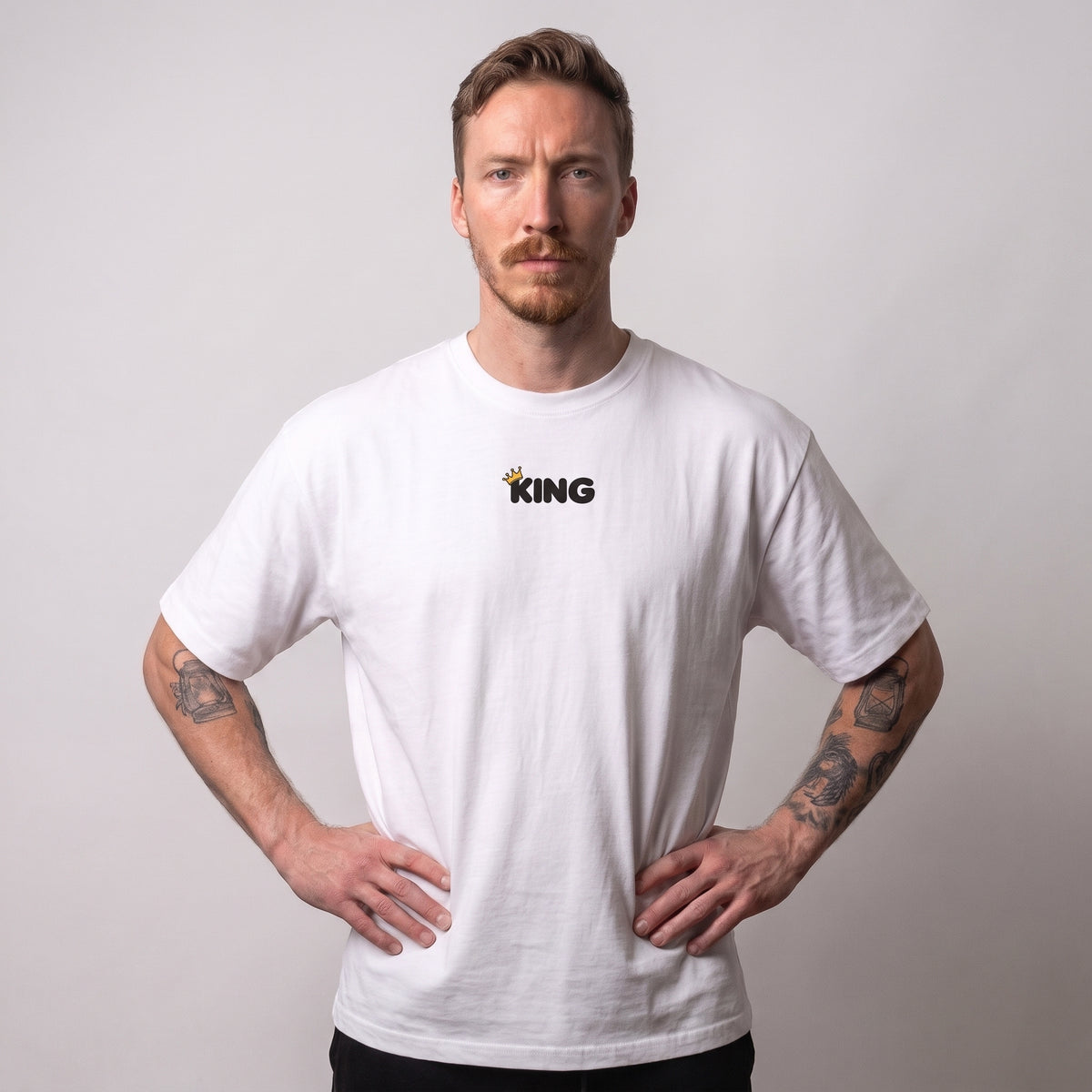 Male model wearing the white KING APEX Look Cute. Lift Heavy. oversized T-shirt, front view showing the black KING chest print with a gold crown.