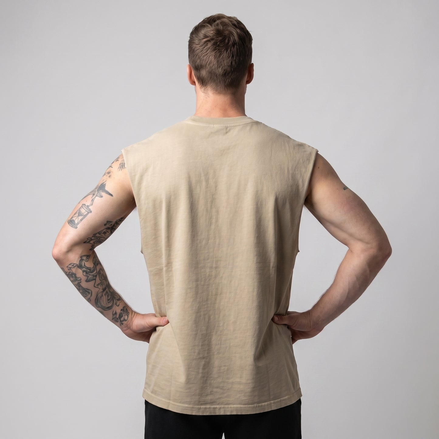 Male model wearing the KING APEX Men's Heavy Faded Tank in Sand Lion, back view with hands on hips.