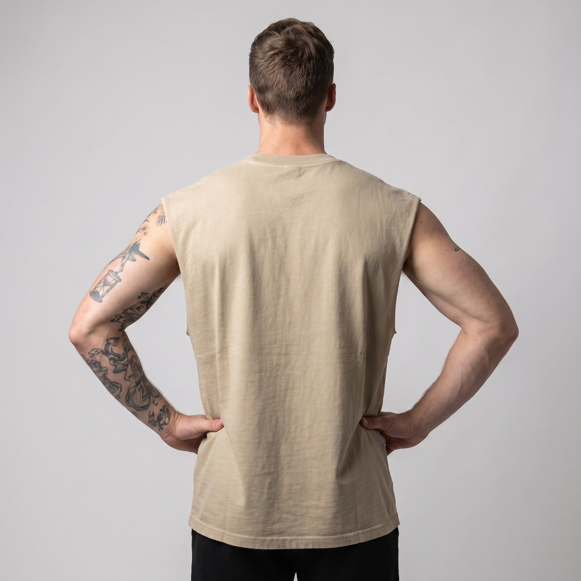 Male model wearing the KING APEX Men's Heavy Faded Tank in Sand Lion, back view with hands on hips.