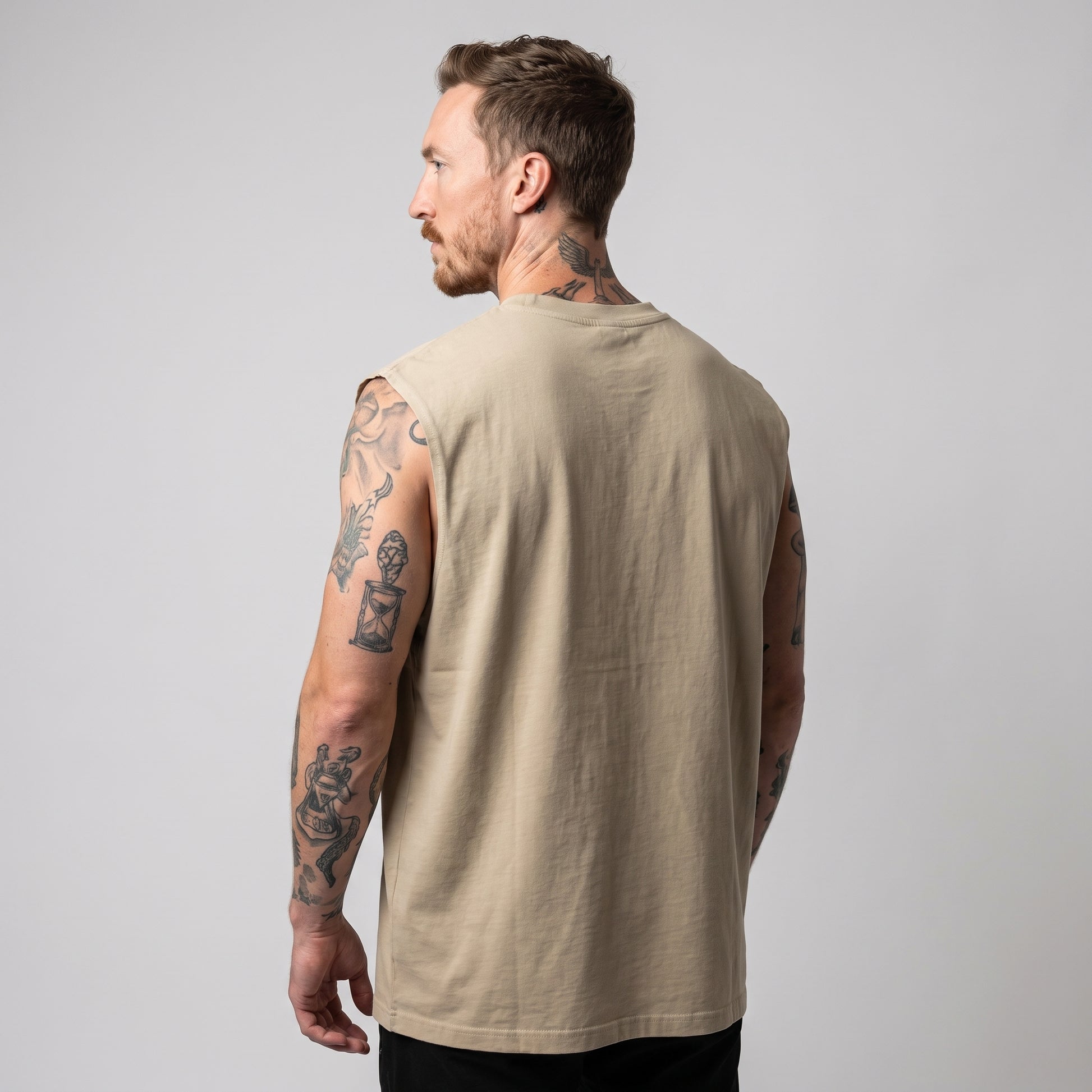 Side profile of a male model wearing the sand KING APEX Heavy Faded Tank, showing its wide armholes and relaxed boxy silhouette.