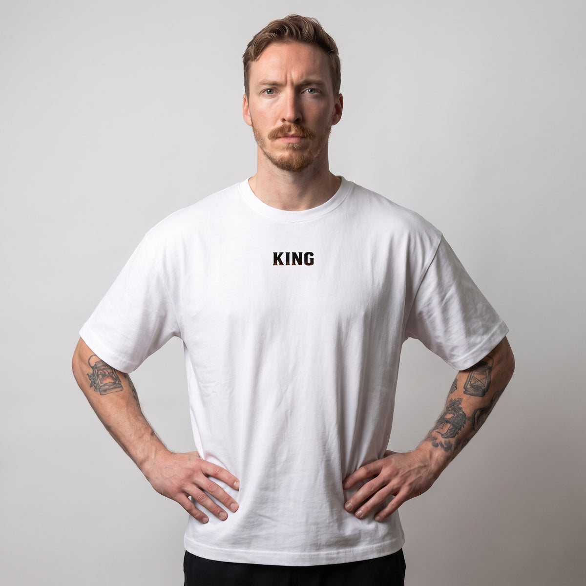 Modèle masculin portant le t-shirt oversize blanc KING APEX No Fear de face, les mains sur les hanches, avec une coupe ample et droite.