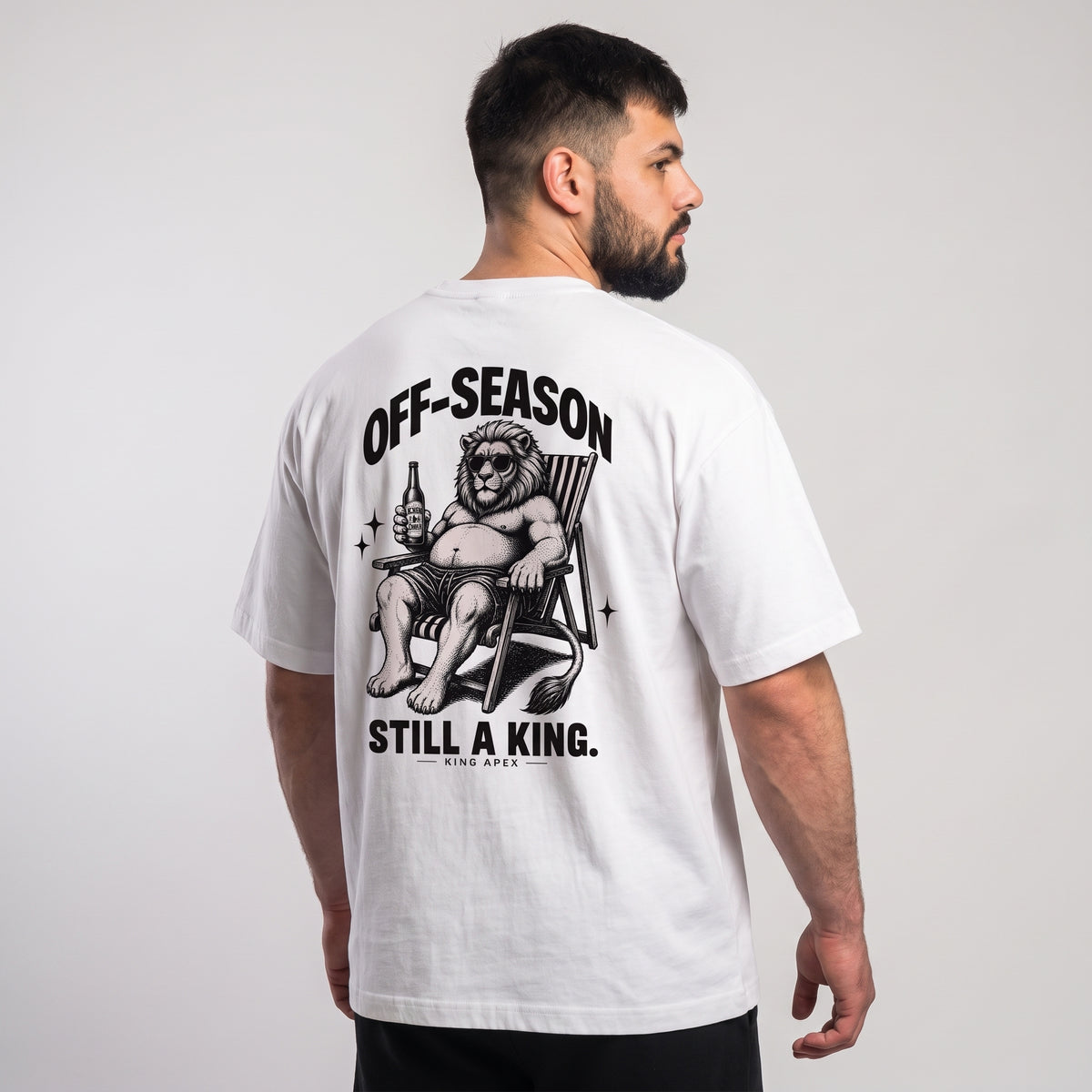 Male model wearing the white KING APEX Off-Season oversized T-shirt, back view showing the black reclining lion artwork with OFF-SEASON and STILL A KING. lettering.