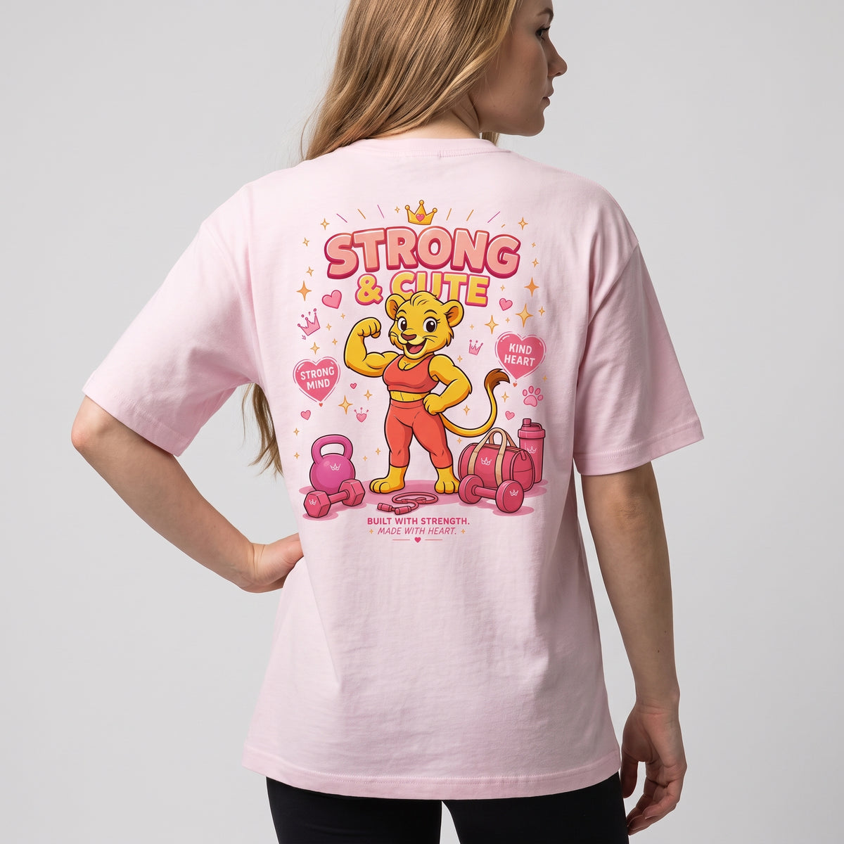 Back view of a woman with hands on hips wearing the KING APEX Soft Pink oversized T-shirt with the Strong & Cute print.