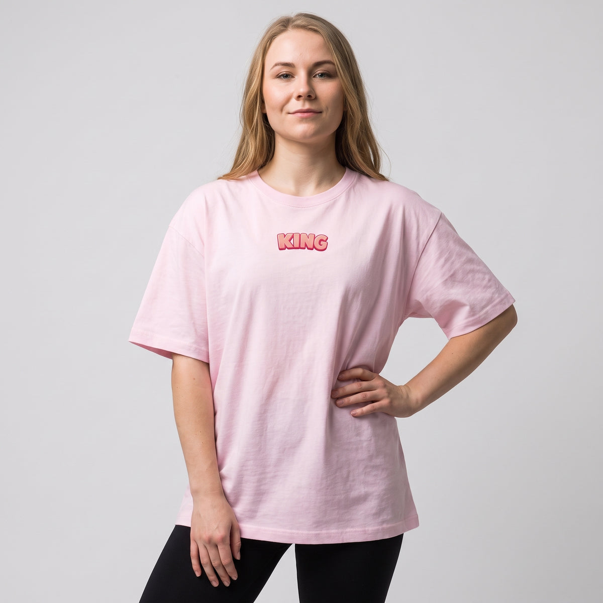 Woman wearing the KING APEX Soft Pink oversized T-shirt, showing its relaxed fit and small pink KING chest print.