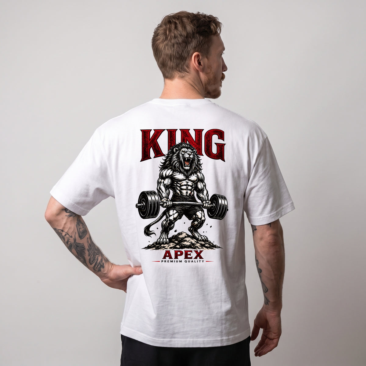 Male model wearing the white KING APEX Power oversized T-shirt, showing the barbell lion graphic and red KING and APEX lettering on the back.