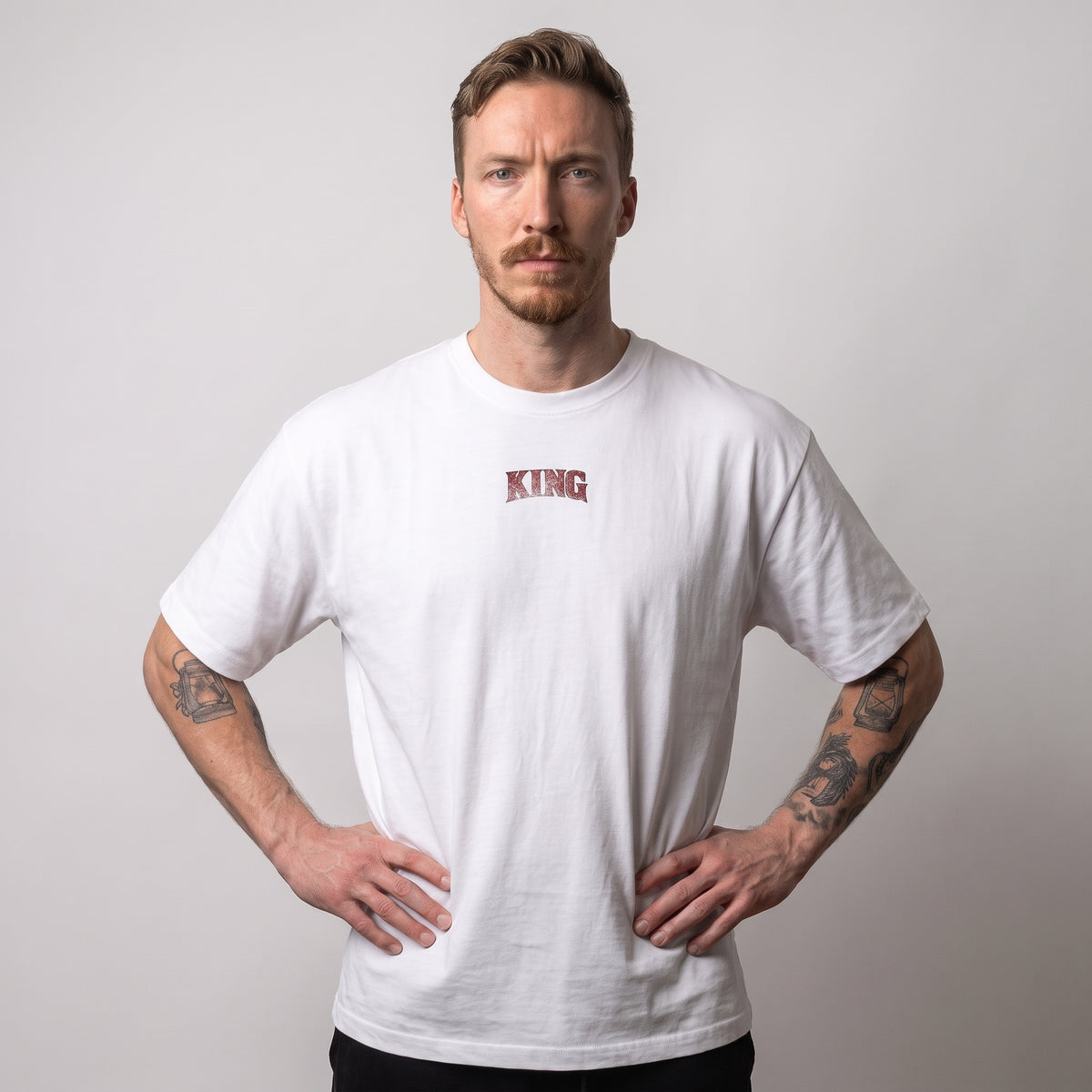 Male model wearing the white KING APEX Power oversized T-shirt, front view with hands on hips and a small red KING chest print.