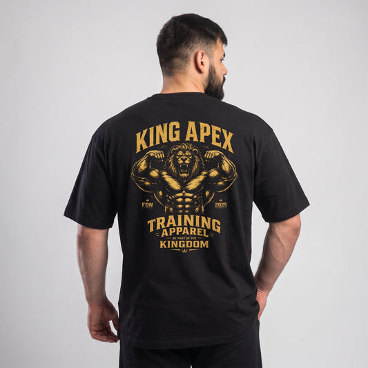 Male model wearing the black KING APEX Training Apparel oversized T-shirt, back view showing the gold flexing lion with KING APEX and TRAINING APPAREL lettering.