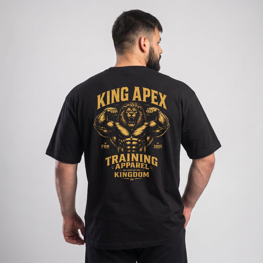 Male model wearing the black KING APEX Training Apparel oversized T-shirt, back view showing the gold flexing lion with KING APEX and TRAINING APPAREL lettering.