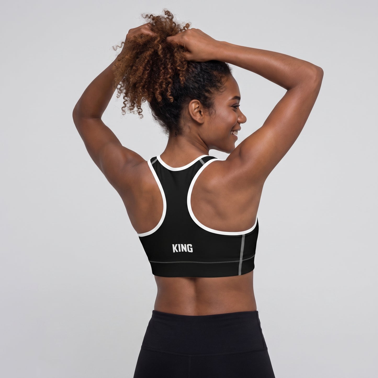 Back view of the KING Lioness Sports Bra in black with white piping on a female model.