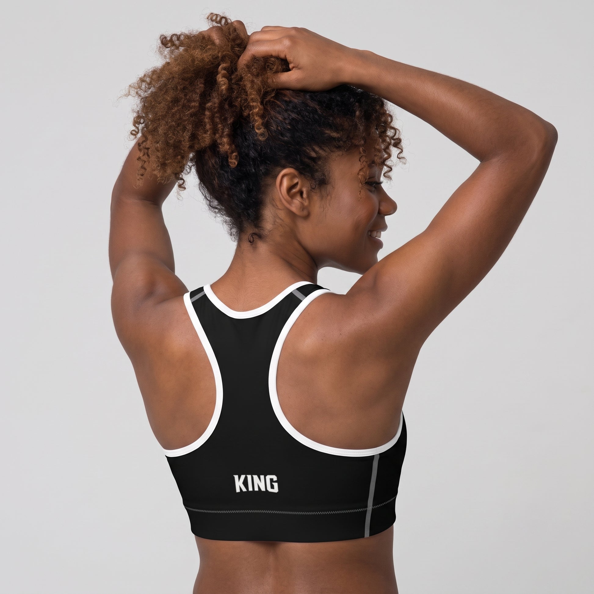 Back view of the KING Lioness Sports Bra in black with white piping on a female model.