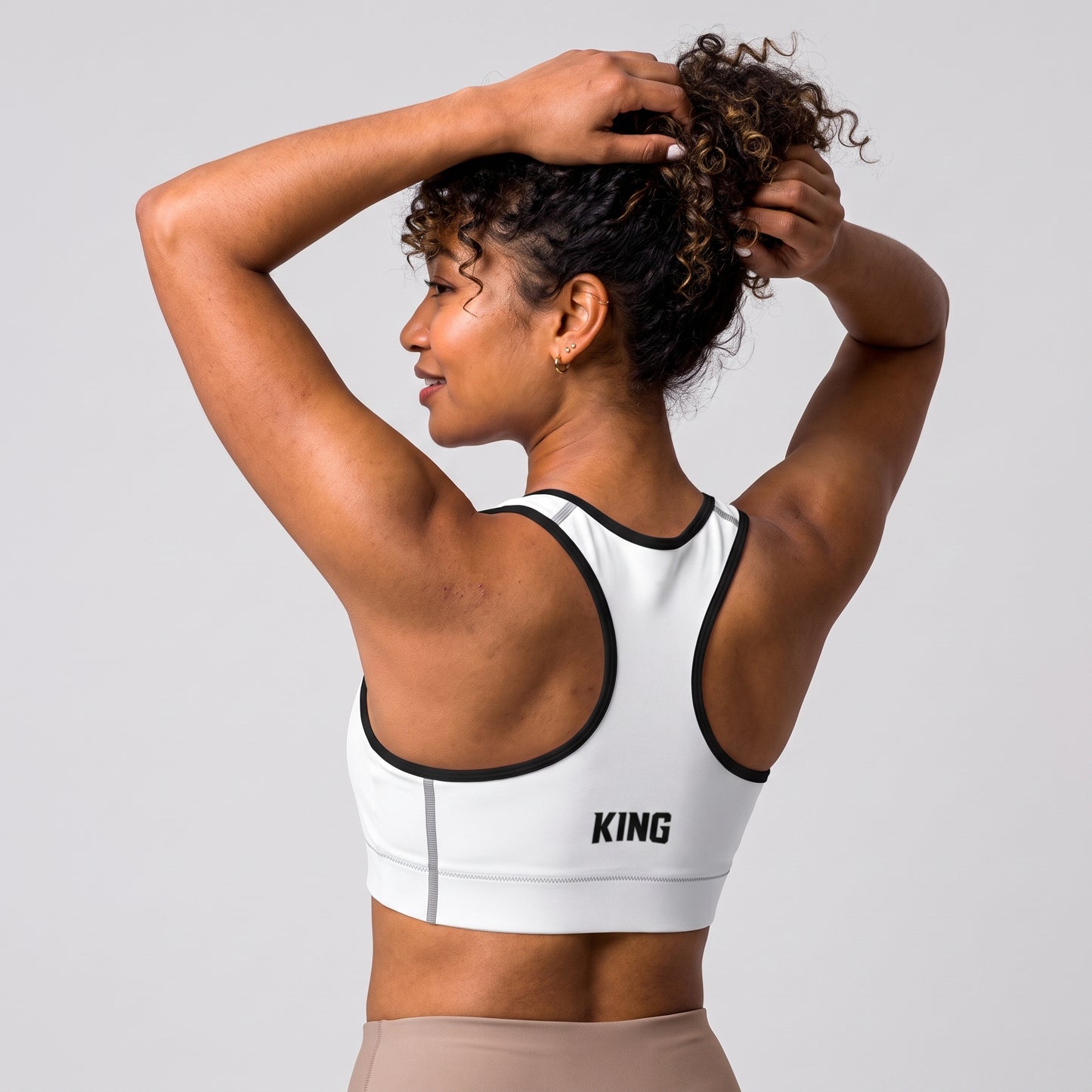 Angled back view of the KING Lioness Sports Bra in white with black piping on a female model.