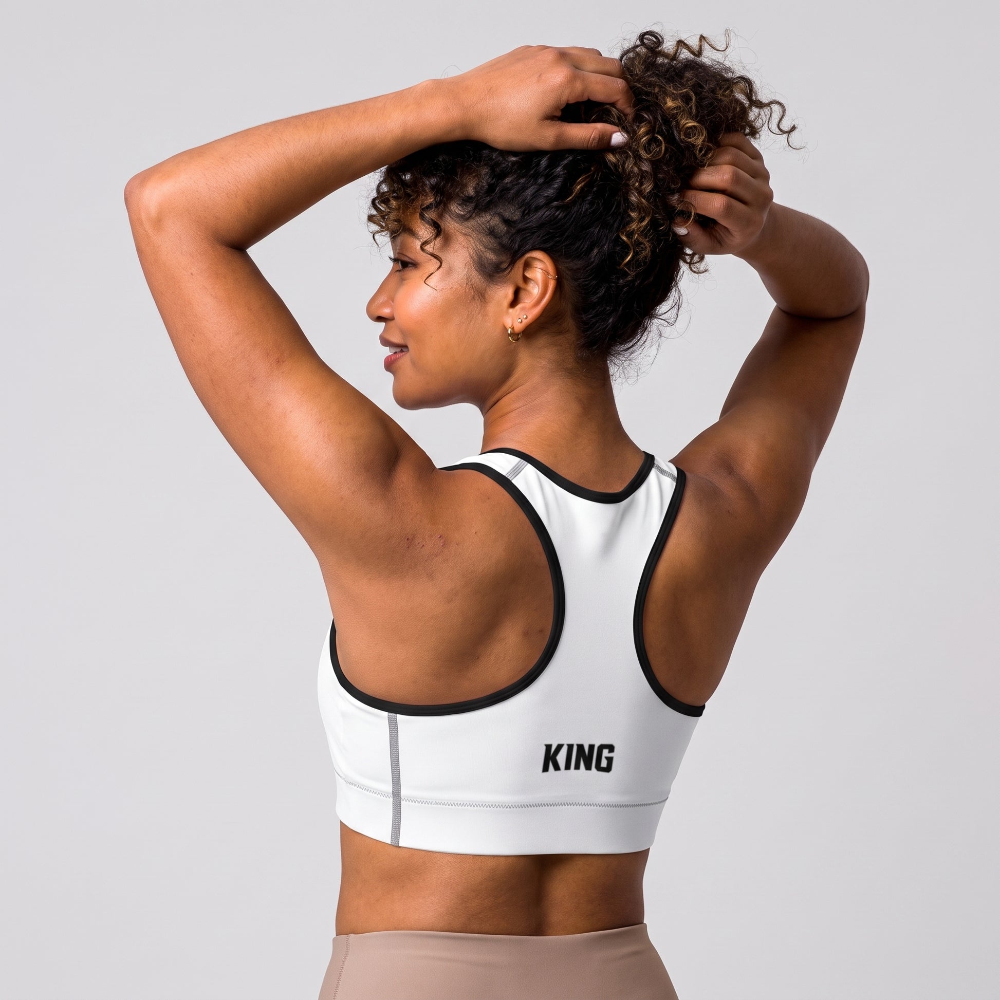 Angled back view of the KING Lioness Sports Bra in white with black piping on a female model.