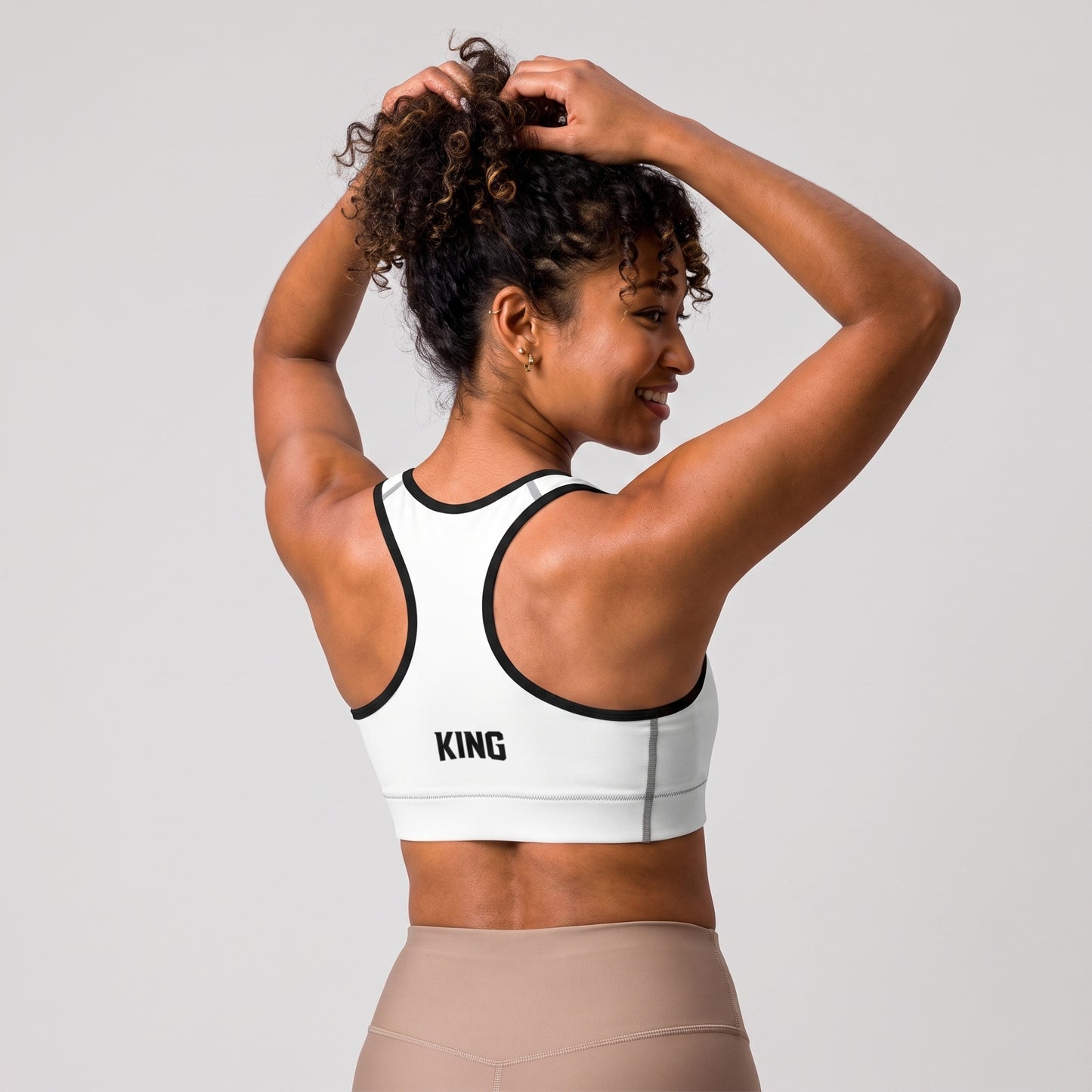 Back view of the KING Lioness Sports Bra in white with black piping on a female model.