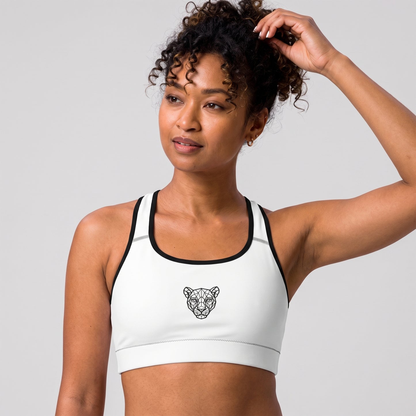 Angled front view of the KING Lioness Sports Bra in white with black piping on a female model.