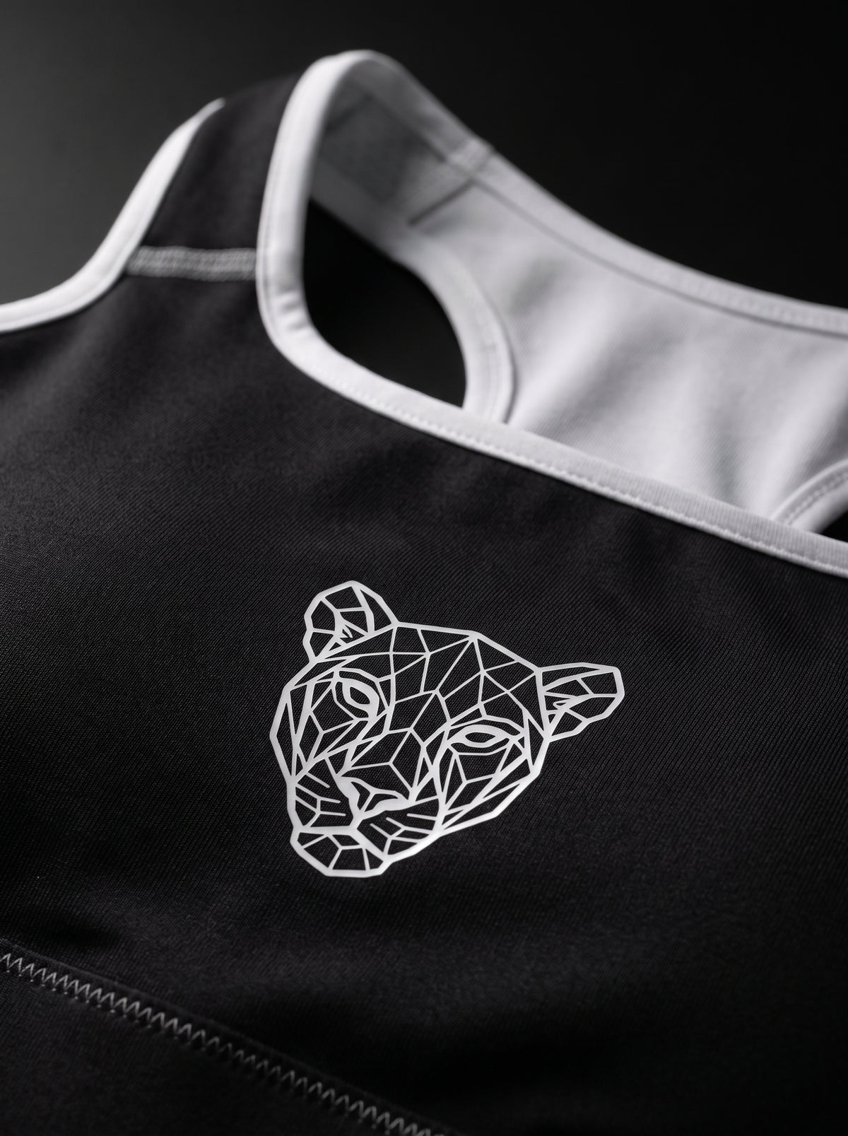 Close-up of the geometric Lioness emblem on a black sports bra with white trim